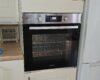 Built-in Hotpoint electric oven in kitchen cabinet showing digital display and control dials
