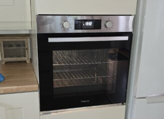 Built-in Hotpoint electric oven in kitchen cabinet showing digital display and control dials