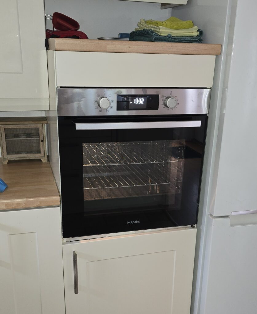 Built-in Hotpoint electric oven in kitchen cabinet showing digital display and control dials